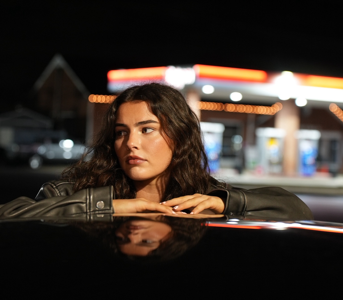 Kailey Jane leaning on a car at a gas station, cinematic